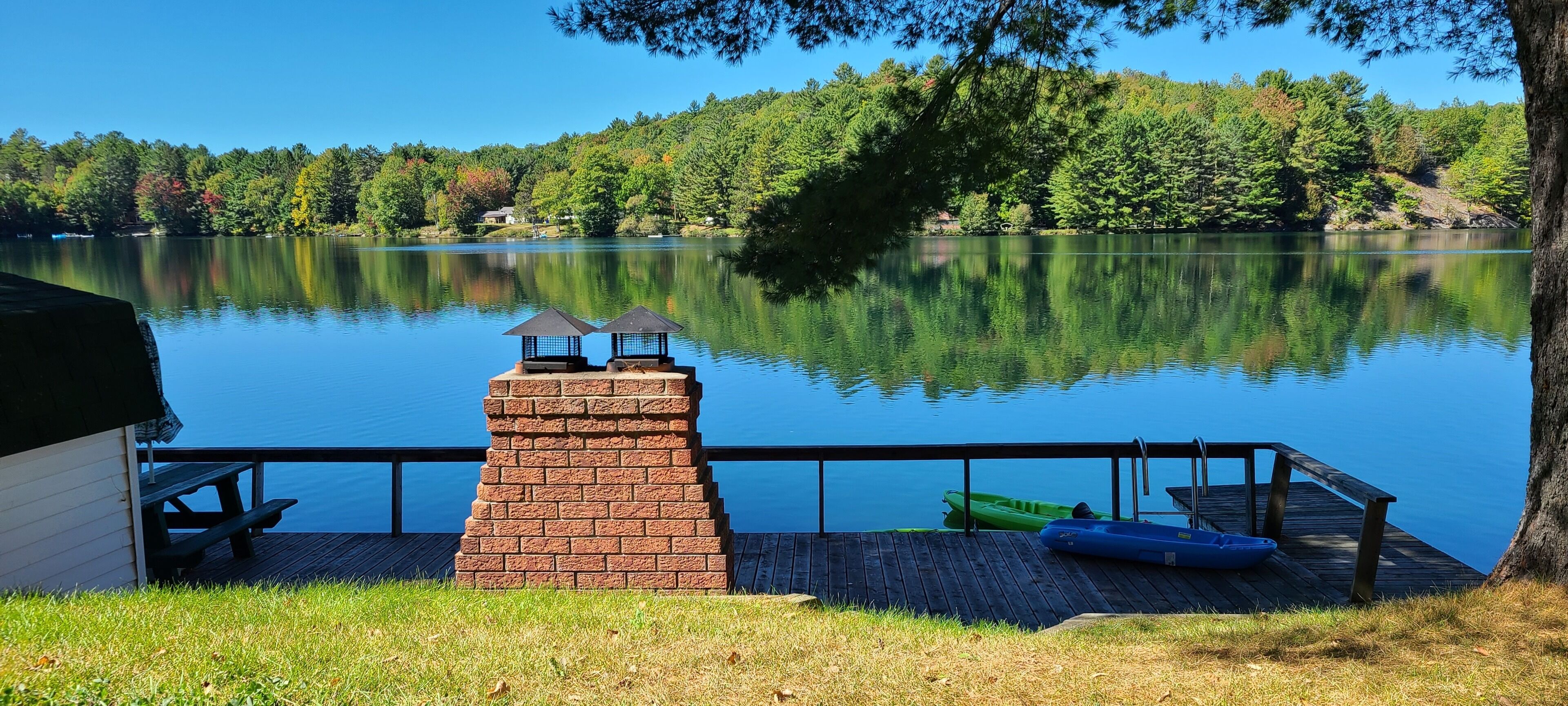 A lakeside deck with a brick chimney, picnic table, and kayak.
