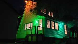 A house with a steep roof and a porch, illuminated by green lights. -  Charming  Cozy  Waterfront Cottage  (Val Des Bois)