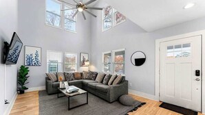 A living room with a sectional sofa, a coffee table, a ceiling fan, and a door with a doormat. - City Oasis with Hot Tub Group-Friendly (Atlanta)