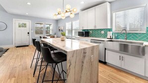 A modern kitchen with a marble island, black bar stools, white cabinets, and a green tiled backsplash. - City Oasis with Hot Tub Group-Friendly (Atlanta)