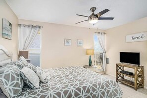 A bedroom with a bed, a ceiling fan, a TV on a wooden stand, and a "beach" sign on the wall.