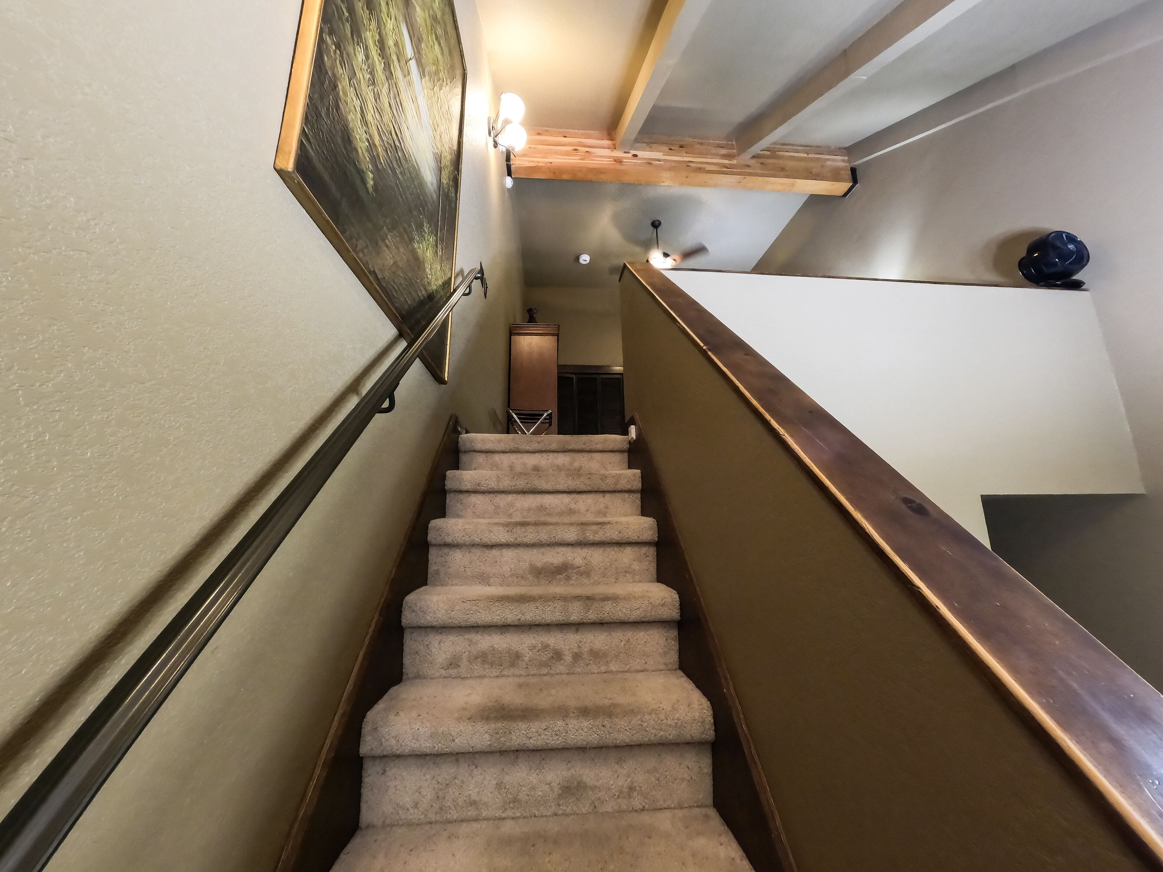 A carpeted staircase with wooden handrails, a wall-mounted light fixture, and a ceiling fan.