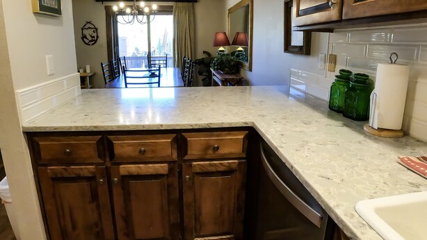 A kitchen with wooden cabinets, a marble countertop, and a view to the dining area. - Epic Mountain Views! 2 Miles North of Purgatory! Heated Pool ! (Durango)