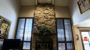A room with a stone fireplace, wooden beams, and a large window with blinds. - Epic Mountain Views! 2 Miles North of Purgatory! Heated Pool ! (Durango)