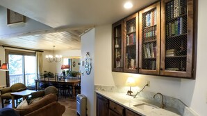 A kitchen with wooden cabinets, a marble countertop, and a dining area with chairs and a table. - Epic Mountain Views! 2 Miles North of Purgatory! Heated Pool ! (Durango)