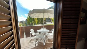 Une terrasse en bois avec une table et des chaises, un grand parasol et une vue sur une région montagneuse.