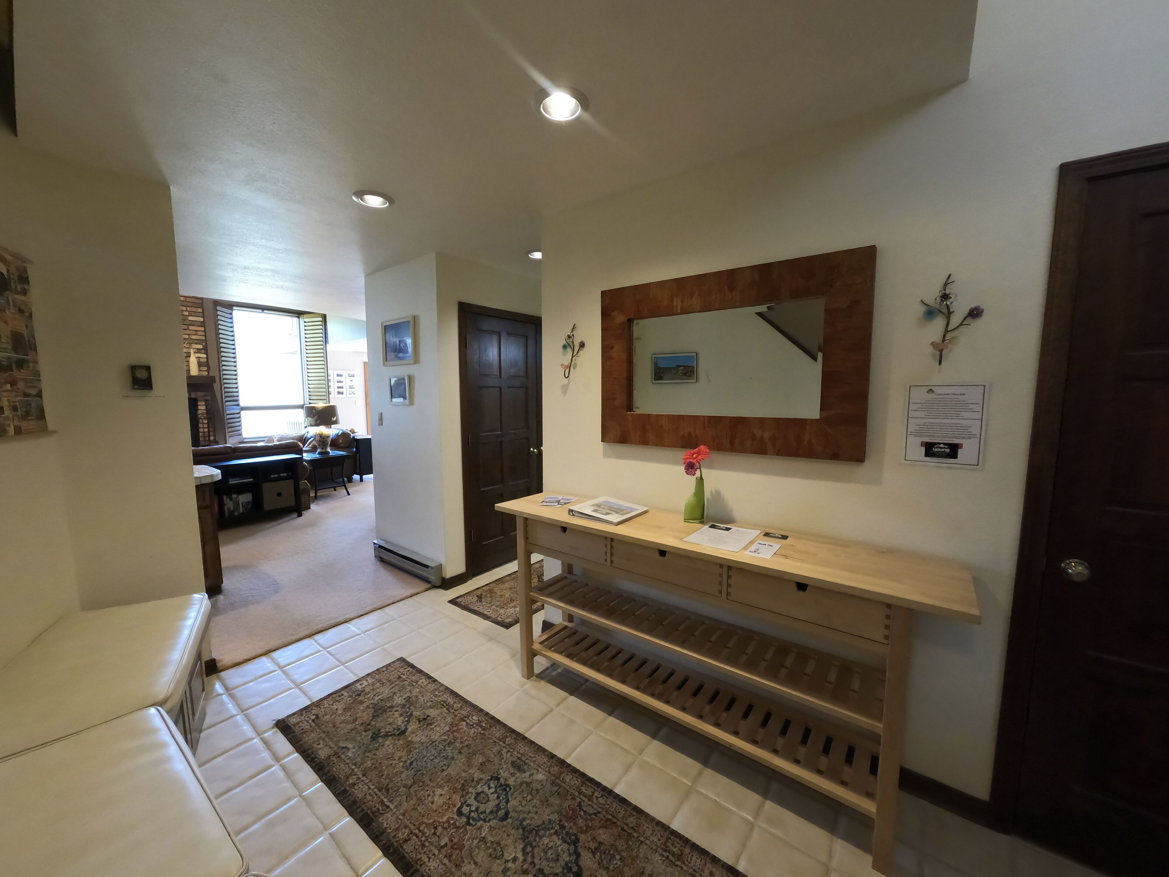A hallway with a wooden bench, a mirror, and a vase with a flower.