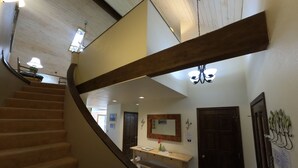 Un escalier avec une rampe en bois menant à un palier où se trouvent une console en bois, une porte et un luminaire fixé au mur.