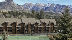 Ein Chalet mit Tennisplatz, umgeben von Bergen und Bäumen.