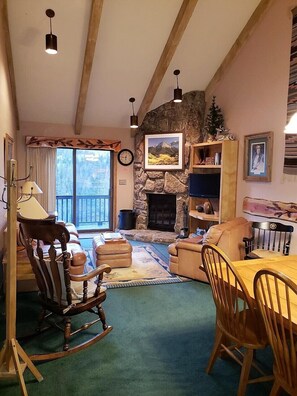 Ein gemütliches Wohnzimmer mit Kamin aus Stein, Holzmöbeln und Blick ins Grüne.