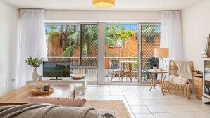Un salon moderne doté d’une grande porte-fenêtre coulissante donnant sur un balcon, d’un canapé, d’une table basse et d’un téléviseur.