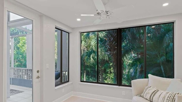 Una habitación con ventanas amplias, ventilador de techo y sofá blanco.
