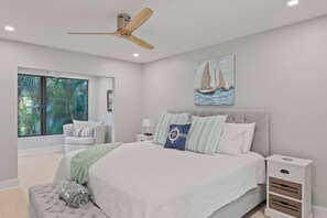 Une chambre Ă coucher comprenant un lit, une table de chevet, une chaise, un ventilateur de plafond et une fenĂȘtre donnant sur un paysage verdoyant.