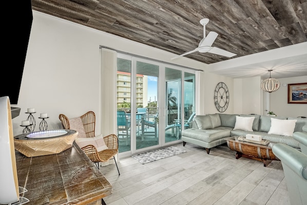 A spacious living room with a large sectional sofa, a wooden coffee table, and a dining area with wicker chairs.