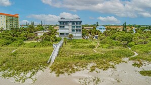 A beachfront property with a multi-story building, a boardwalk leading to the beach, and surrounding greenery. - Turtle Beach Beachview Condo - Beautifully updated - Private - Quiet Ocean View (Cocoa Beach)