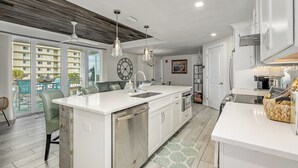A modern kitchen with a central island, white cabinetry, and a large window overlooking a balcony. - Turtle Beach Beachview Condo - Beautifully updated - Private - Quiet Ocean View (Cocoa Beach)