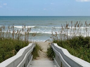 A wooden boardwalk leading to a beach with waves and seaweed.