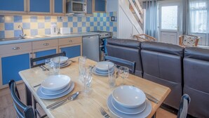 A compact kitchen with blue cabinets, a microwave, and a dishwasher. There is a dining table set with plates, glasses, and cutlery. A leather booth is visible in the background.