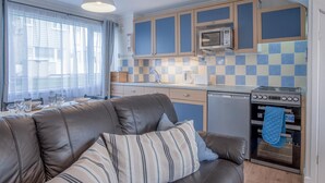 A compact kitchen with a microwave, oven, and sink. There is a sofa with striped cushions in the living area.