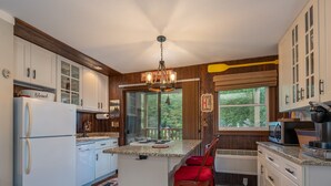 A kitchen with wooden cabinets, a refrigerator, a dining area with a bear-themed chair, and a view of the outdoors.