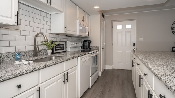 A modern kitchen with white cabinets, granite countertops, a stainless steel sink, a microwave, and a coffee maker.