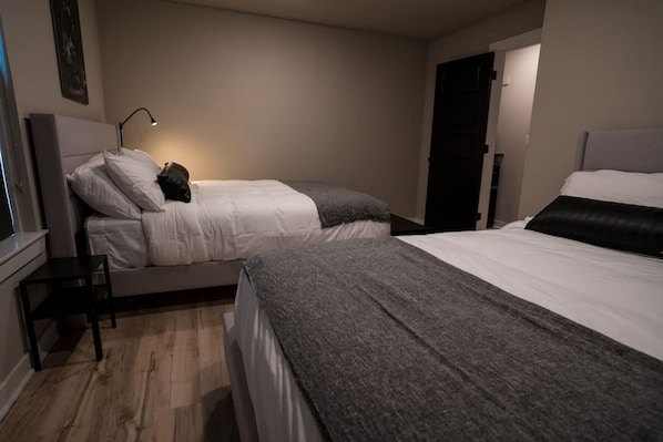 Une chambre avec deux lits, une table de chevet, une lampe et une porte.