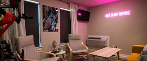 Een kamer met twee stoelen, een tafeltje, een tv aan de muur en een neonbord.
