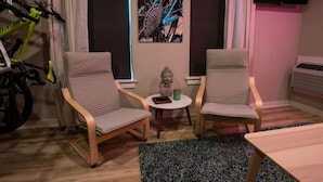 Ein Zimmer mit zwei Stühlen, einem kleinen Tisch, einem Fahrrad und einem am Wand montierten Fernseher.