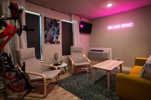 A modern living room with two armchairs, a small table, and a yellow sofa. There is a bicycle in the corner, a painting on the wall, and a neon sign. - The Bike Inn #1, Devils Den Double Suite (Bentonville)