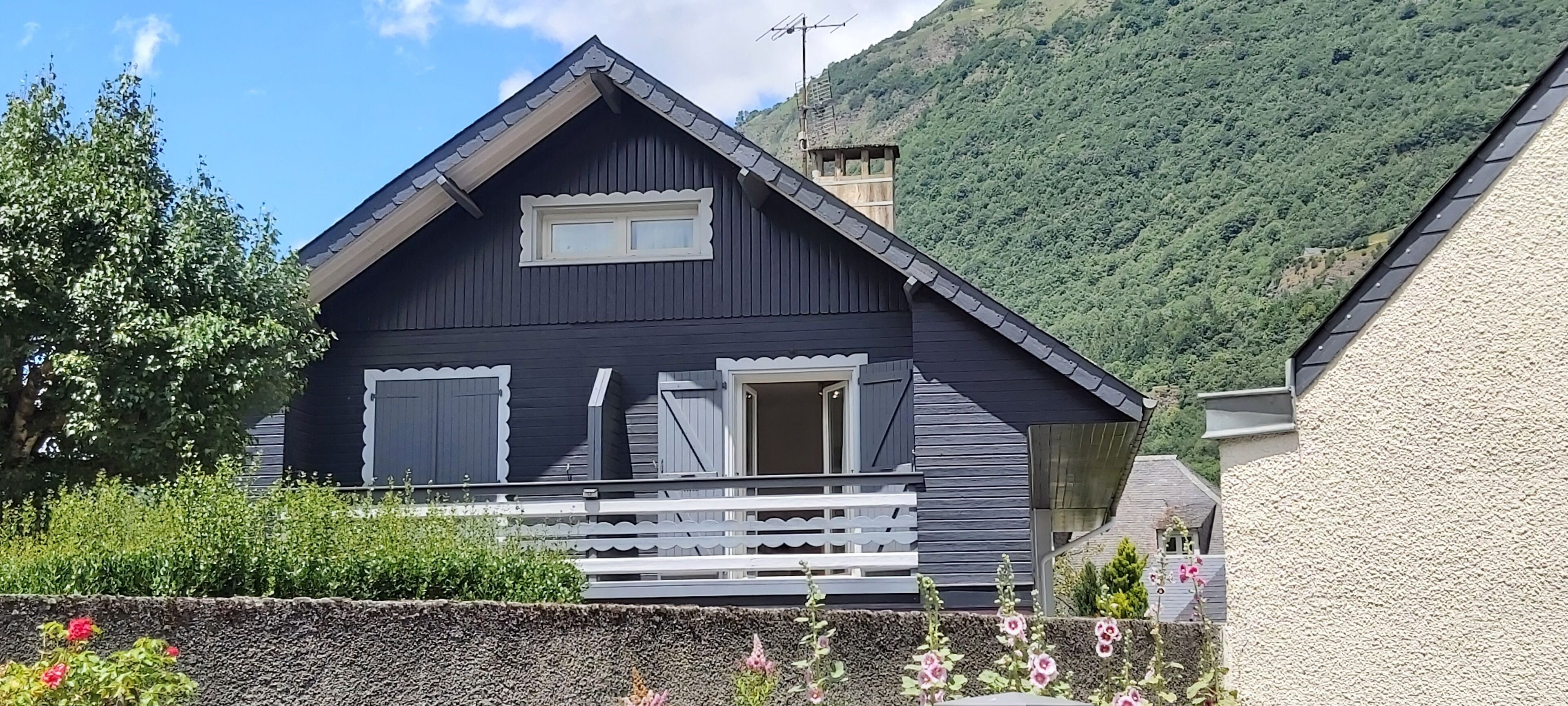 Une maison en bois de couleur sombre, avec un toit à pignon, un petit balcon et une fenêtre.