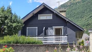 Une maison en bois de couleur sombre, avec un toit à pignon, un petit balcon et une fenêtre.