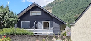 A dark-colored wooden house with a gabled roof, a small balcony, and a window.