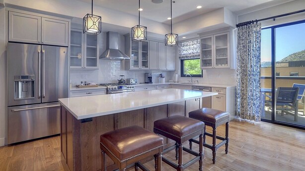 A modern kitchen with stainless steel appliances, a large island with bar stools, pendant lighting, and a view to a balcony. - Downtown Penthouse Condo (Durango)