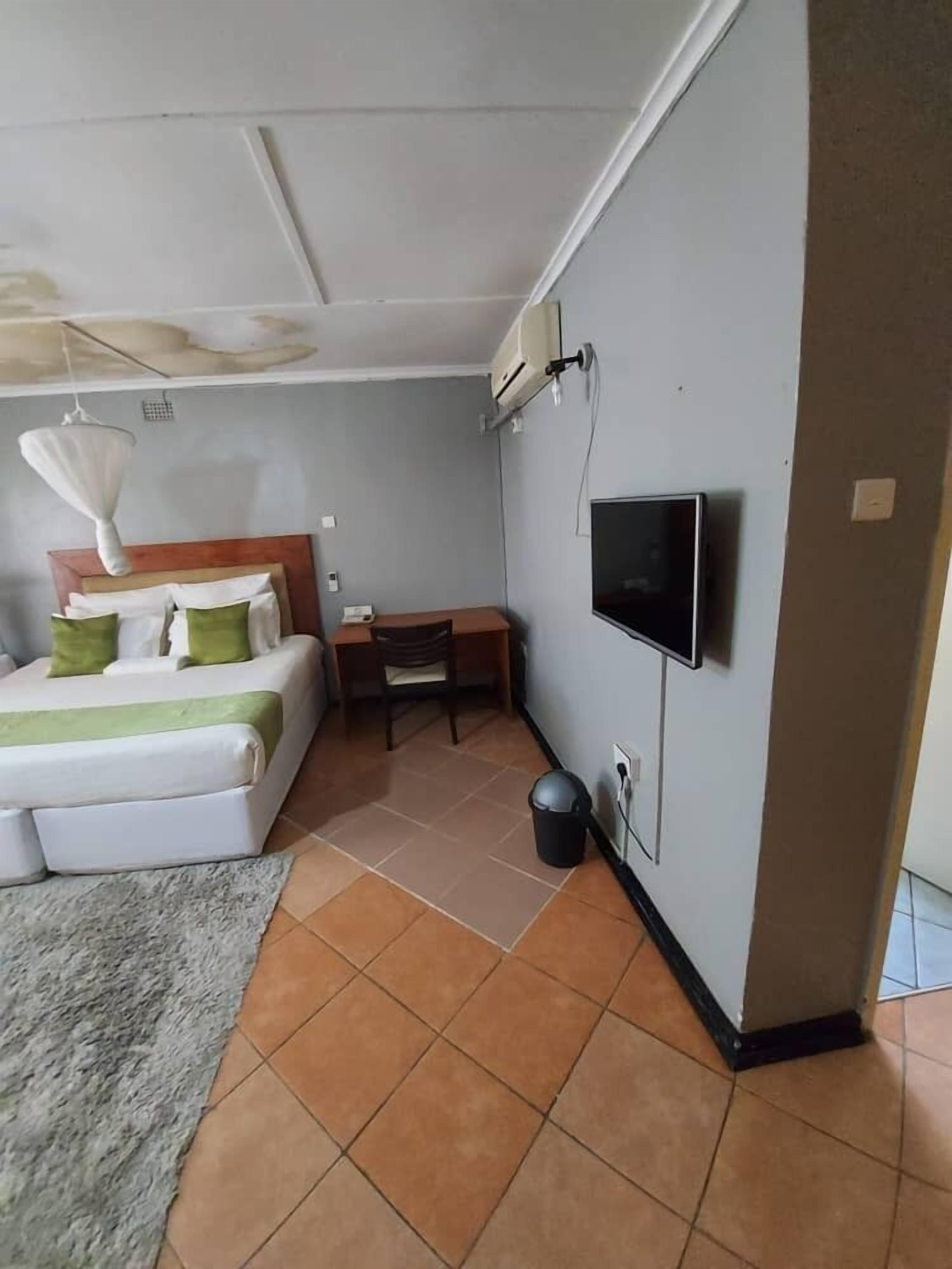 Habitación de hotel con cama, escritorio, silla, televisión y basurero.