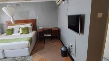 Habitación de hotel con cama, escritorio, silla, televisión y basurero.