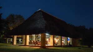 Una estructura con techo de paja y un frente abierto, posiblemente un restaurante o cafetería, con sillas y mesas visibles en su interior.
