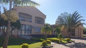 Un edificio de diseño moderno, con un amplio ventanal y un jardín ajardinado con palmeras y arbustos.