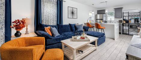 A modern living room with a blue sofa, orange armchair, and a wooden coffee table.