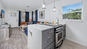 A modern kitchen with a central island, built-in oven, and a dining area with a sofa and table. - NEW Steps to Downtown • 7 Mins to Beach + Parking (New Port Richey)