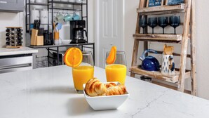 A kitchen with a marble countertop, two glasses of orange juice, a bowl of croissants, and a coffee machine. - NEW Steps to Downtown • 7 Mins to Beach + Parking (New Port Richey)