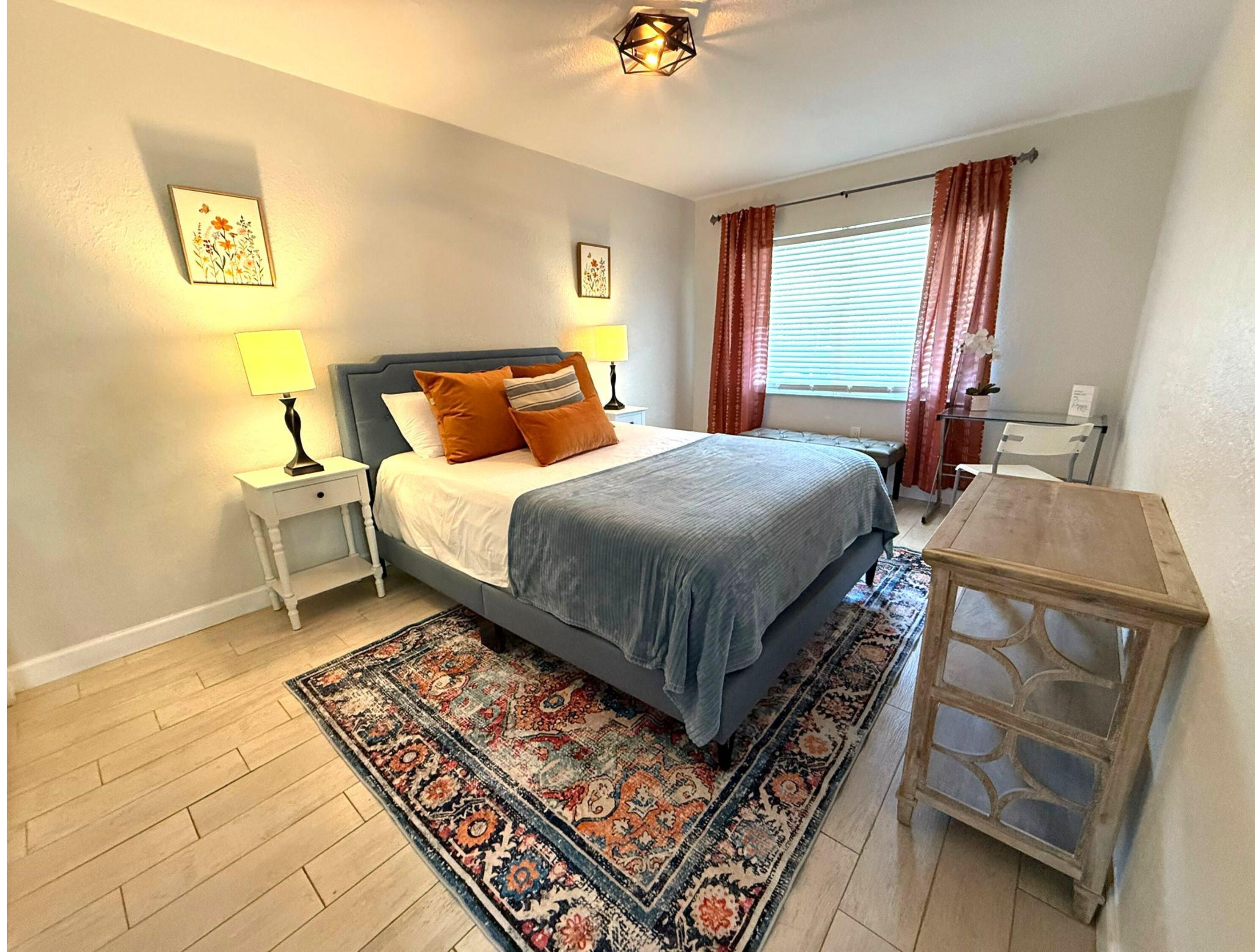 A bedroom with a bed, bedside tables, a desk, and a window with curtains.
