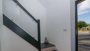 A staircase with a dark handrail and white walls, leading to a door with a view of a garden. - Frith Green (Bromyard)