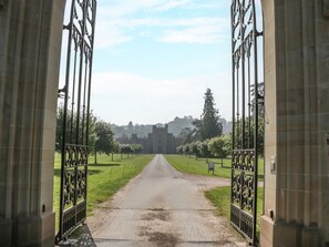 A pathway leading to a castle-like structure with ornate metal gates and a clear sky. - Frith Green (Bromyard)