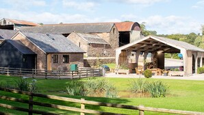 A rustic farmstead with stone buildings, a wooden fence, and a covered outdoor seating area. - Frith Green (Bromyard)