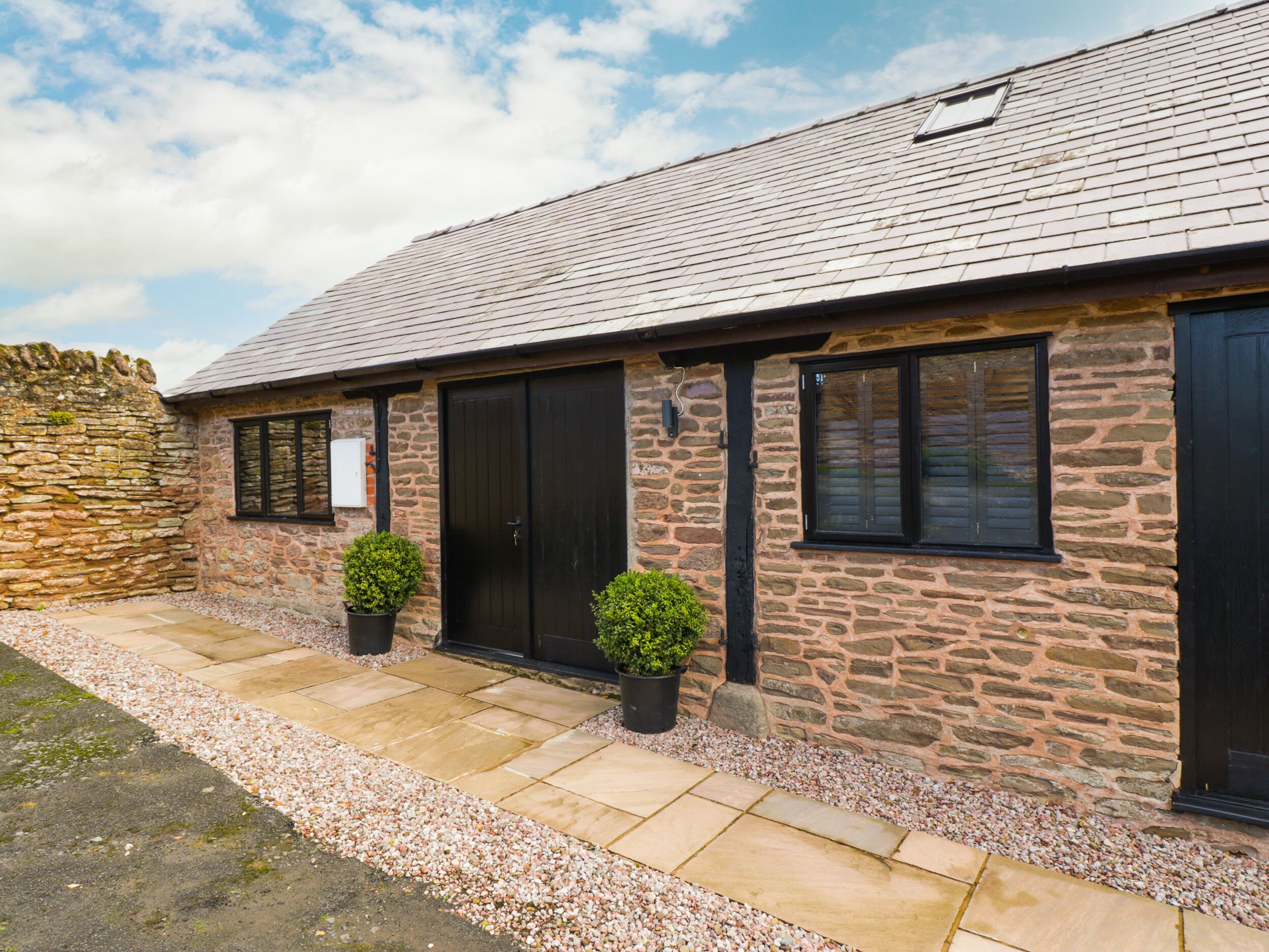 A stone building with a tiled roof, two potted plants, and a gravel pathway.