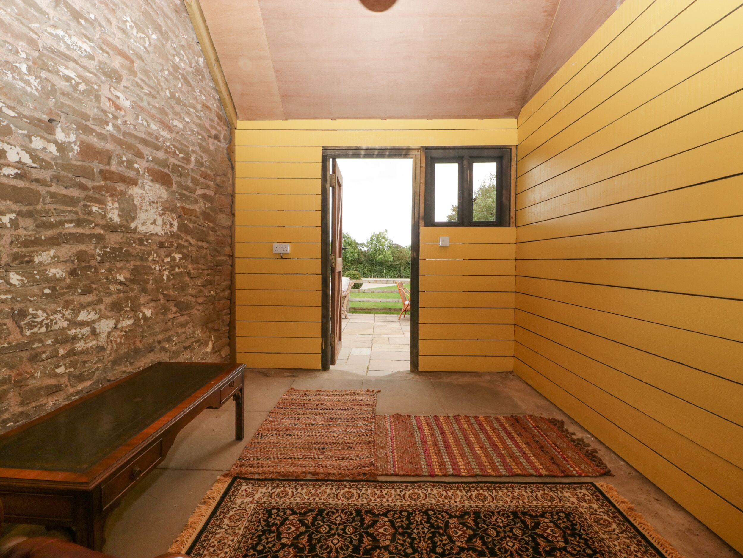 A hallway with yellow walls, a wooden bench, and a rug.