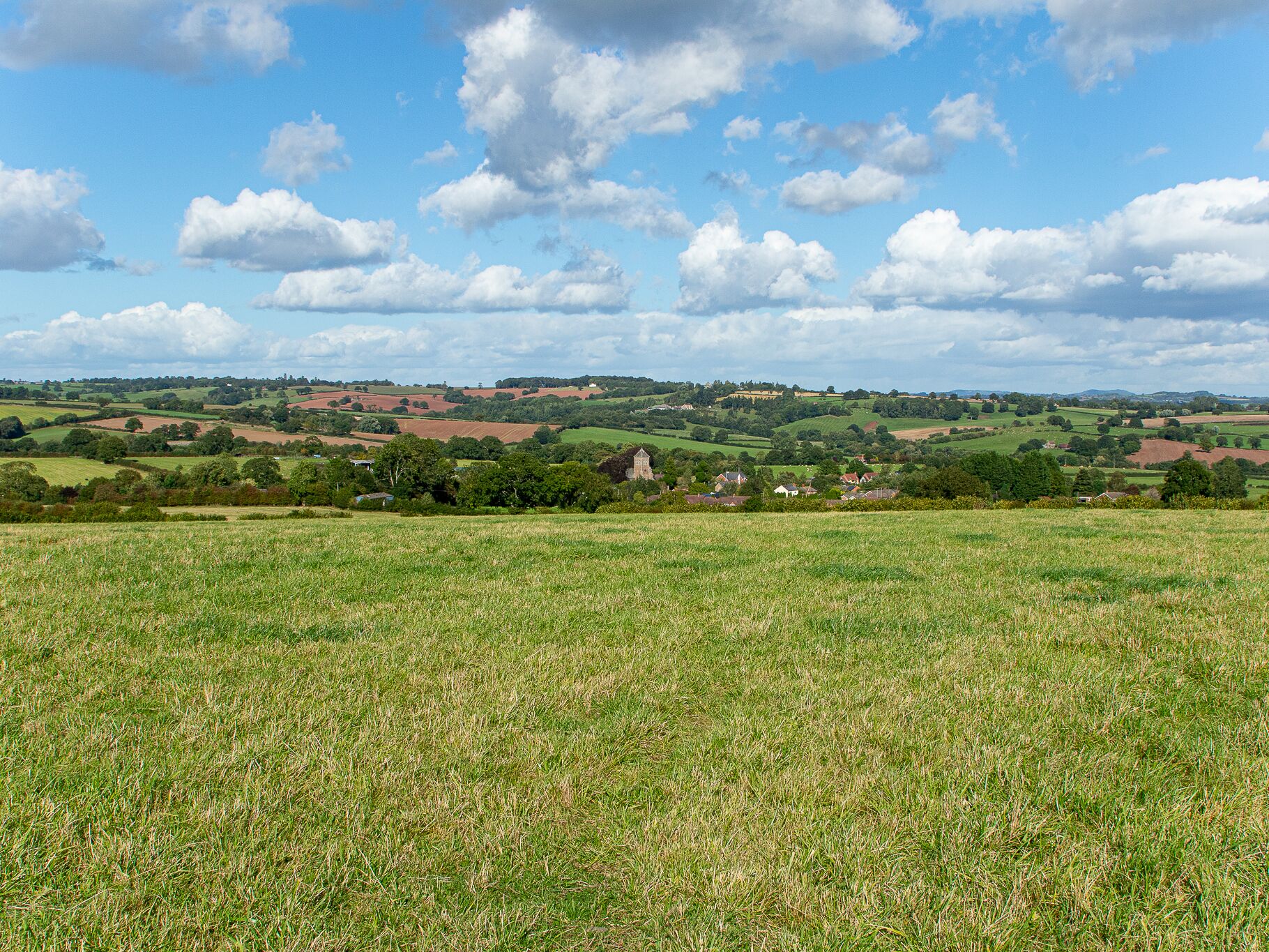 Ländliche Landschaft mit sanften Hügeln, verstreuten Häusern und blauem Himmel.