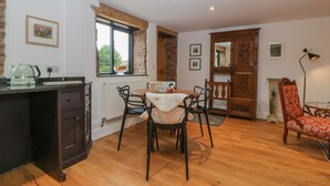A dining area with a wooden table, chairs, and a radiator. There is a window with a view of greenery outside. - Frith Green (Bromyard)