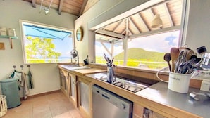 A kitchen with a dishwasher, a window with a view of a green landscape, and a wooden ceiling. - Chambre dans Villa Casa Blue, piscine, vue mer (Cole Bay)