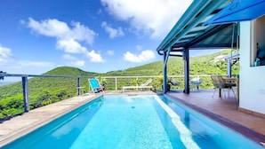 A swimming pool with a view of green hills, a covered seating area, and a clear blue sky. - Chambre dans Villa Casa Blue, piscine, vue mer (Cole Bay)